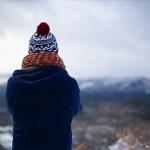 Person in wooly hat and scarf looking out at a snowy landscape