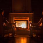 Two people sitting in chairs in front of a roaring fire