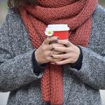 A woman in warm clothing warming her hands around a mug of hot drink